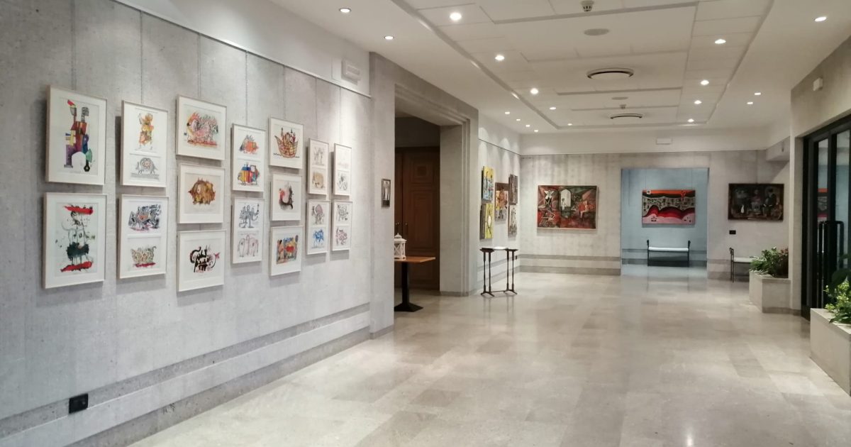 Fotografija galerije KCL Bratuz, z vhodom in številnimi slikami na stenah.