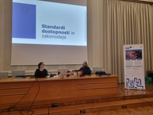 Fokus na predavatelja, na platnu napis "Standardi dostopnosti in zakonodaja"