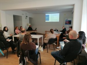 Pogled na udeležence, v ospredju predstavnik osnovne šole, ki zastavlja vprašanje, v ozadju predavatelj.