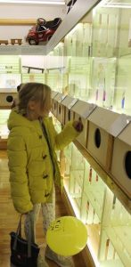 Obiskovalka s tipanjem v tipni škatli odkriva igračo, ob njej rumen balon.