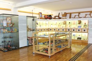 Razstavni prostor s taktilnimi oznakami, tipnimi škatlami in vitrino z igračami.