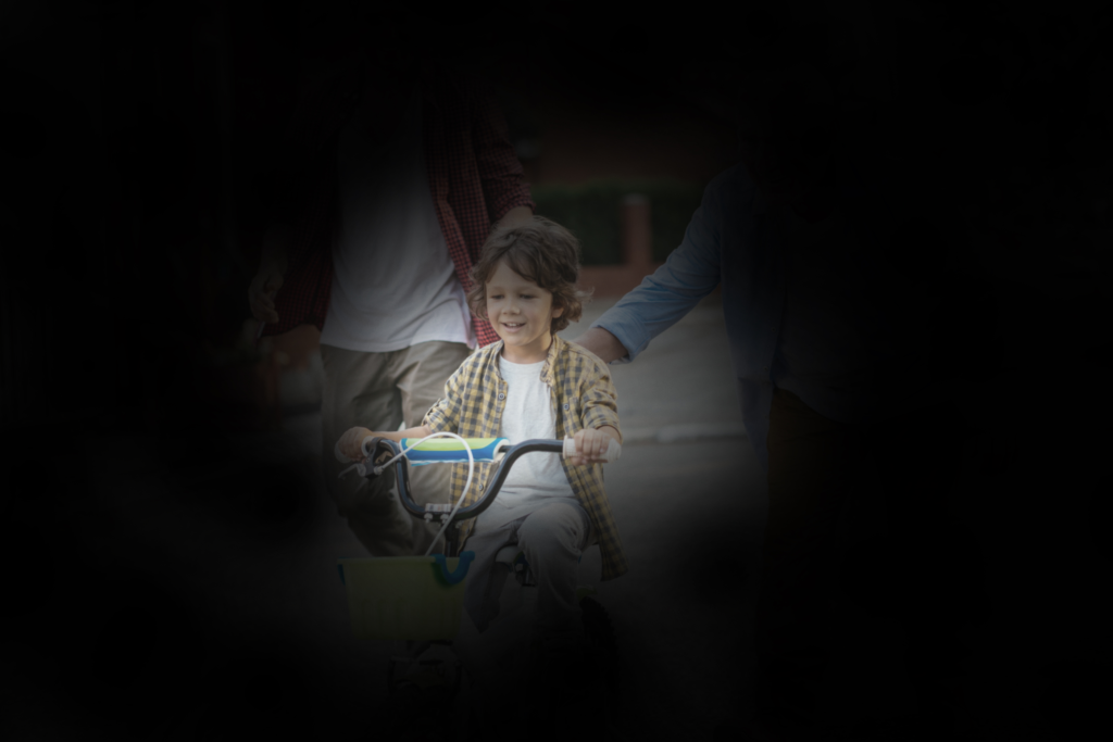 Otrok se vozi s kolesom, vidno je le ozko osrednje območje, robovi so temni (simulacija retinitis pigmentosa).