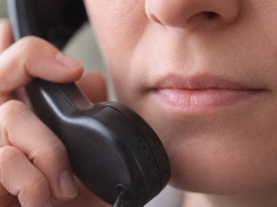 Bližnji posnetek osebe z zaprtimi usti, ki drži telefonsko slušalko ob obrazu.