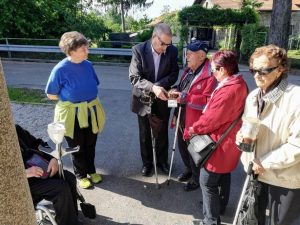 Skupina starejših na prostem; nekateri imajo bele palice in tipajo manjše etnološke predmete.