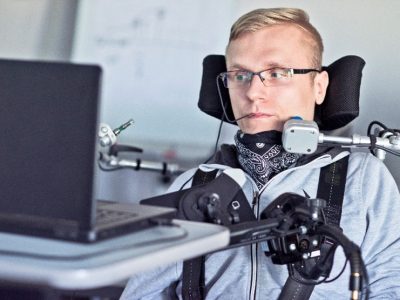 Oseba uporablja voziček ter stikala in druge podporne naprave za upravljanje računalnika.