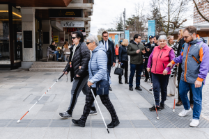 Več oseb z belimi palicami prečka mestno ulico po taktilnih vodilnih oznakah med usposabljanjem za samostojno orientacijo.