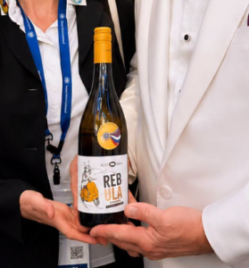 Steklenica vina Rebula, ki jo dve osebi držita v rokah.