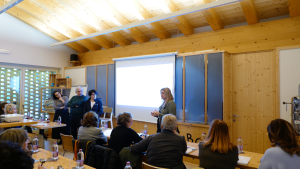 Un gruppo di partecipanti a una formazione ascolta la relatrice che presenta i contenuti davanti a uno schermo di proiezione.