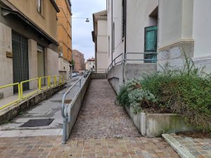 Dostopna rampa s kovinskimi ograjami vodi do vhoda v stavbo.