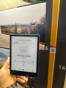 E-bralnik z audiovodnikom pred tablo z informacijami o meji med Slovenijo in Italijo.
